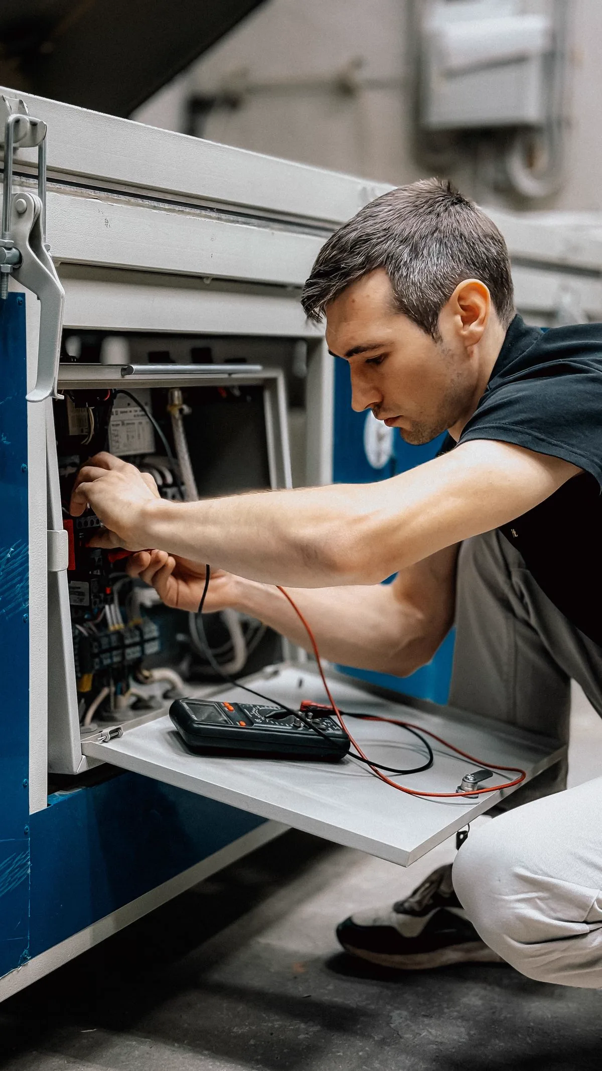 Technician using a multimeter to inspect an industrial control panel